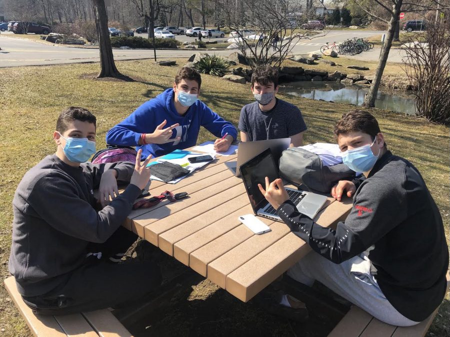 A group of students conversing outdoors while wearing masks and remaining socially distant.