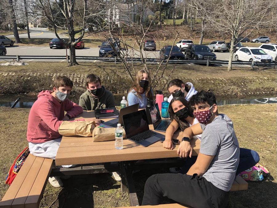 Students enjoying a lunch period outdoors while wearing masks and spending time with one another. 